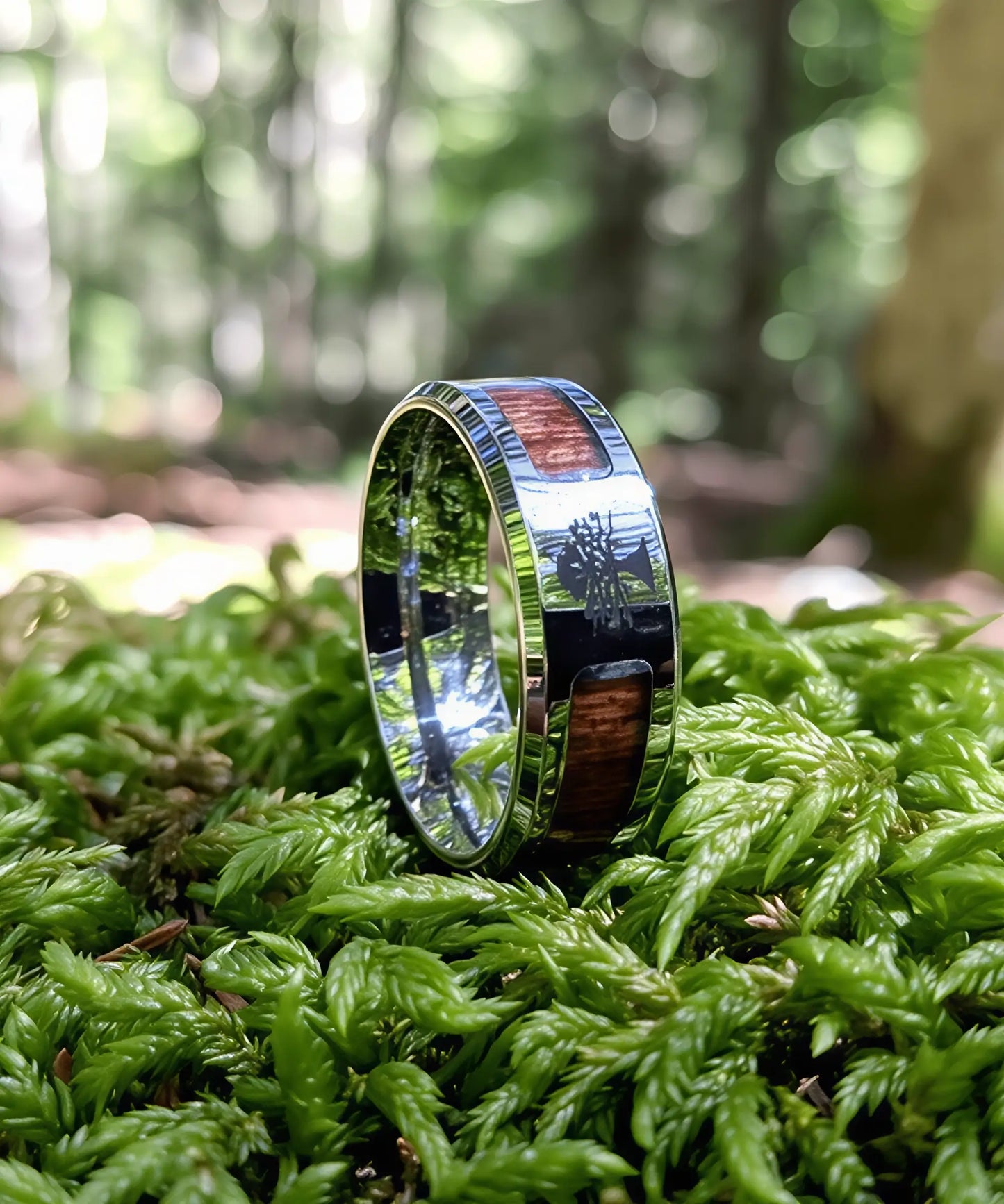Bague Arbre de Vie en bois et acier inoxydable posée sur un tapis de mousse verte en forêt, alliance élégante et naturelle.