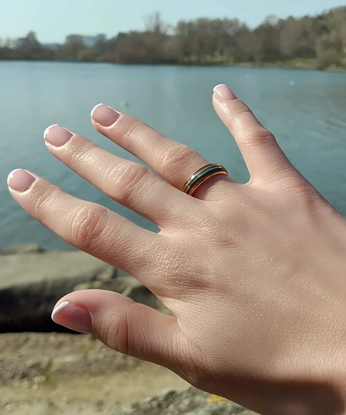 Bague en bois Ark en or jaune avec incrustation turquoise portée à la main en extérieur près d’un lac