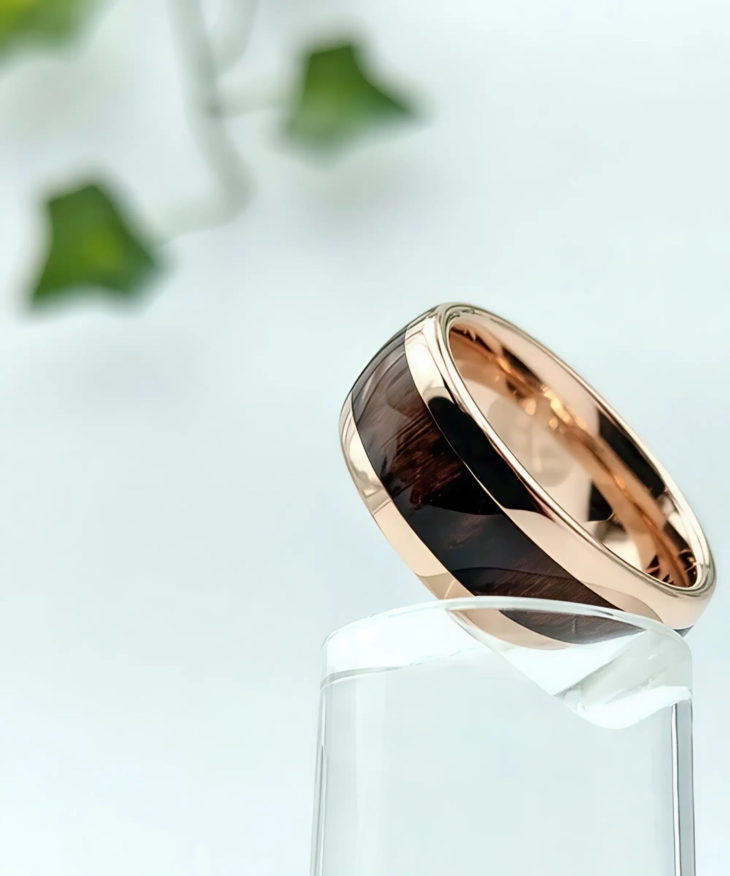 Bague en bois Elior Révo ornée de bois sombre et cerclée d’acier rose doré, présentée en équilibre sur un support en verre transparent