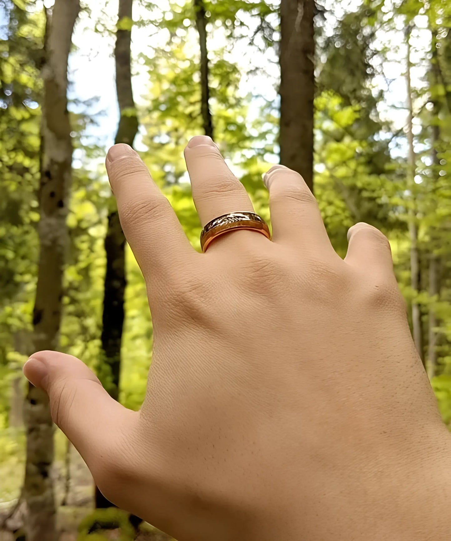 Main portant la bague Flèche de Cupidon Rose Passion en bois et tungstène doré rose, photographiée en forêt parmi les arbres