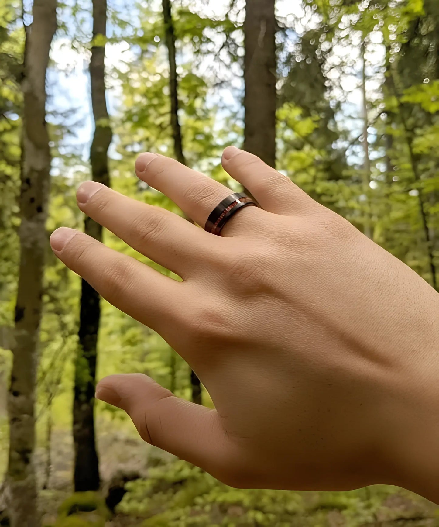 Bague homme en tungstène noir brossé avec incrustation de bois rouge Ultron, portée à la main dans une forêt
