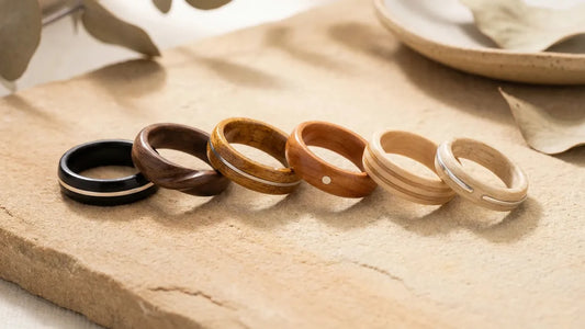 Collection de bagues en bois de différentes essences : ébène, noyer, koa, cerisier, érable et frêne, alignées sur pierre naturelle
