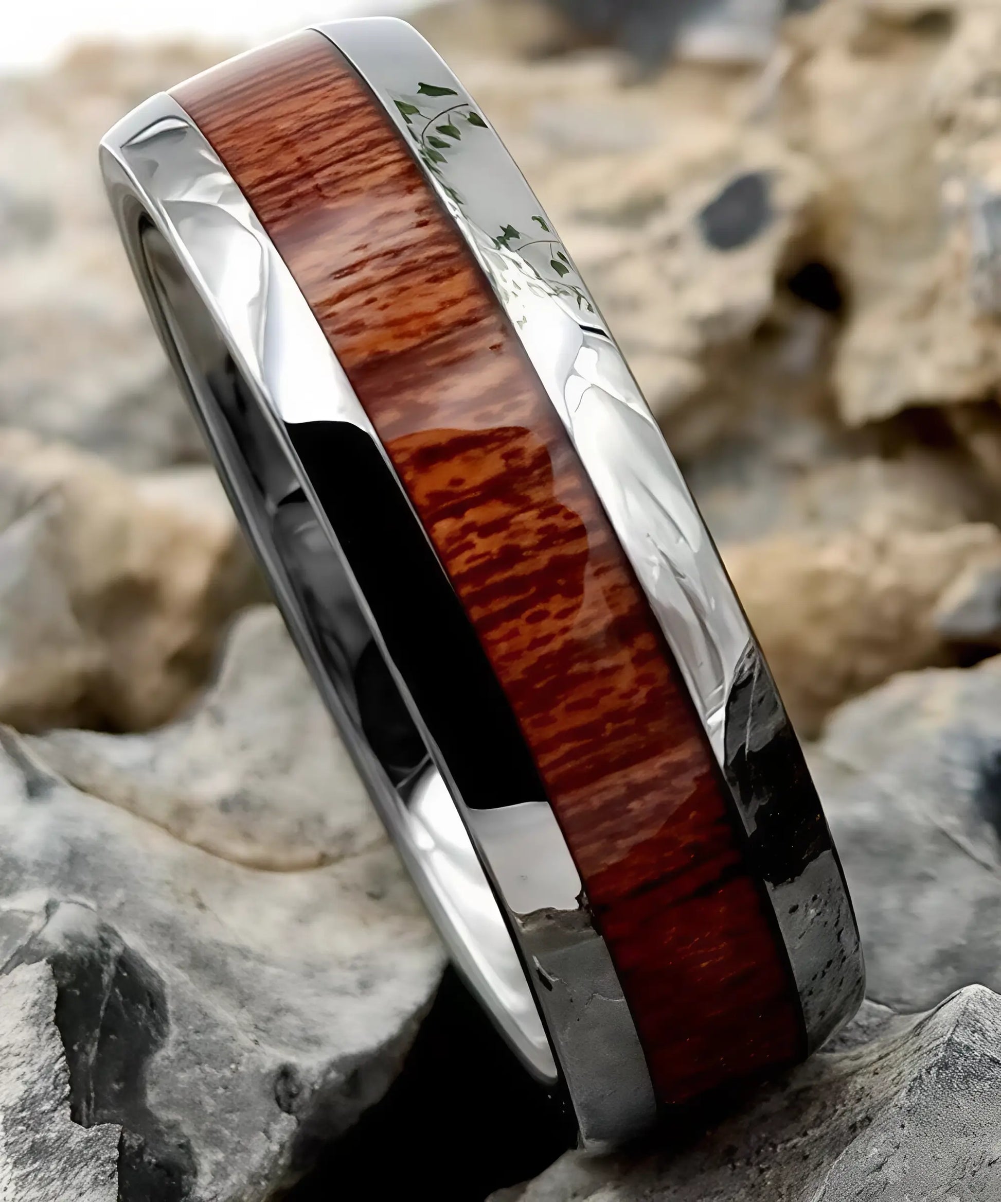 Gros plan sur la bague en bois et argent Elior Klimt, alliance en tungstène argenté avec incrustation de bois raffiné aux reflets rouges, mise en valeur sur des rochers.