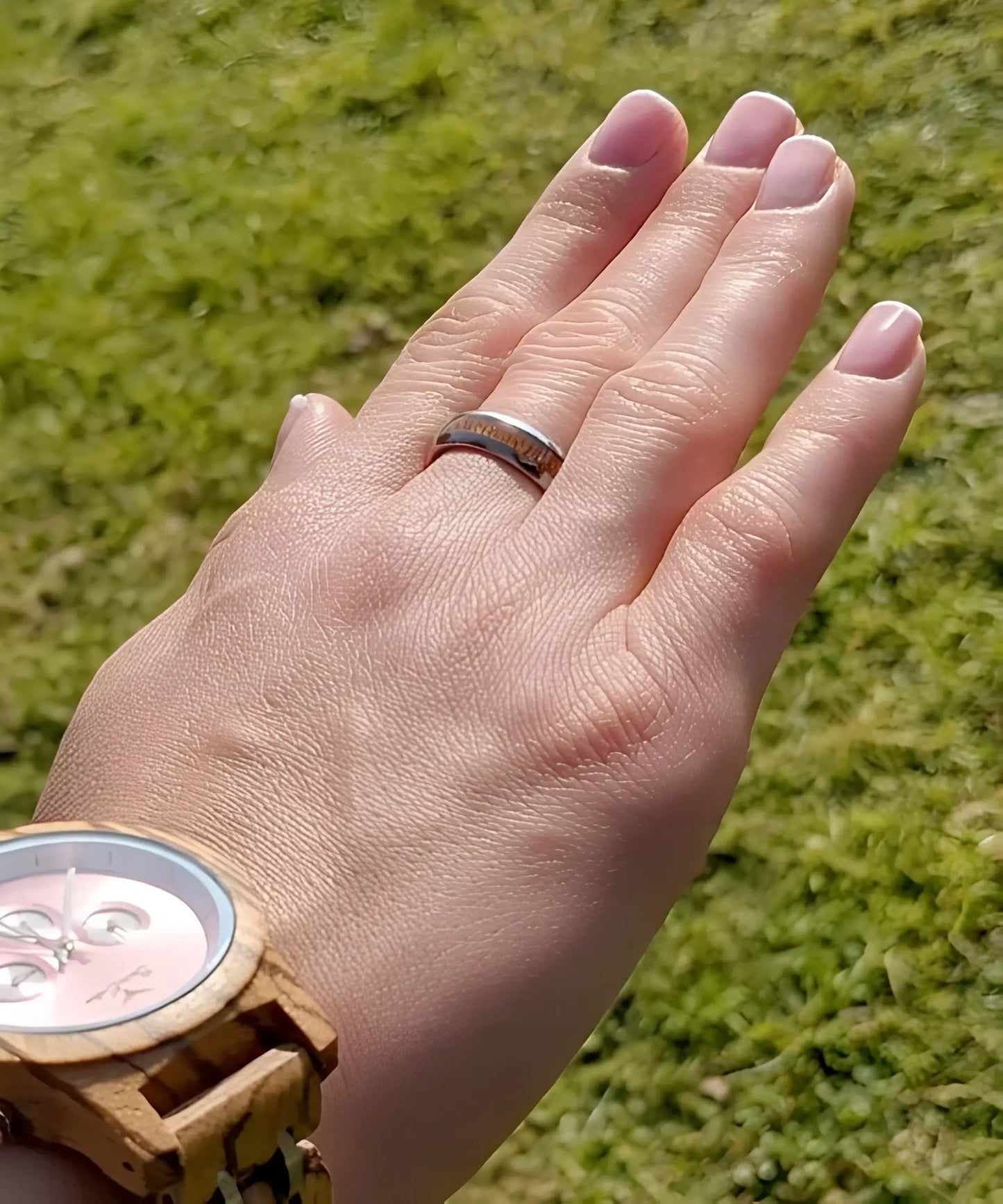 Main de femme portant la bague en bois et argent Elior Klimt, alliance en tungstène argenté avec incrustation de bois raffiné, photographiée en extérieur au soleil.