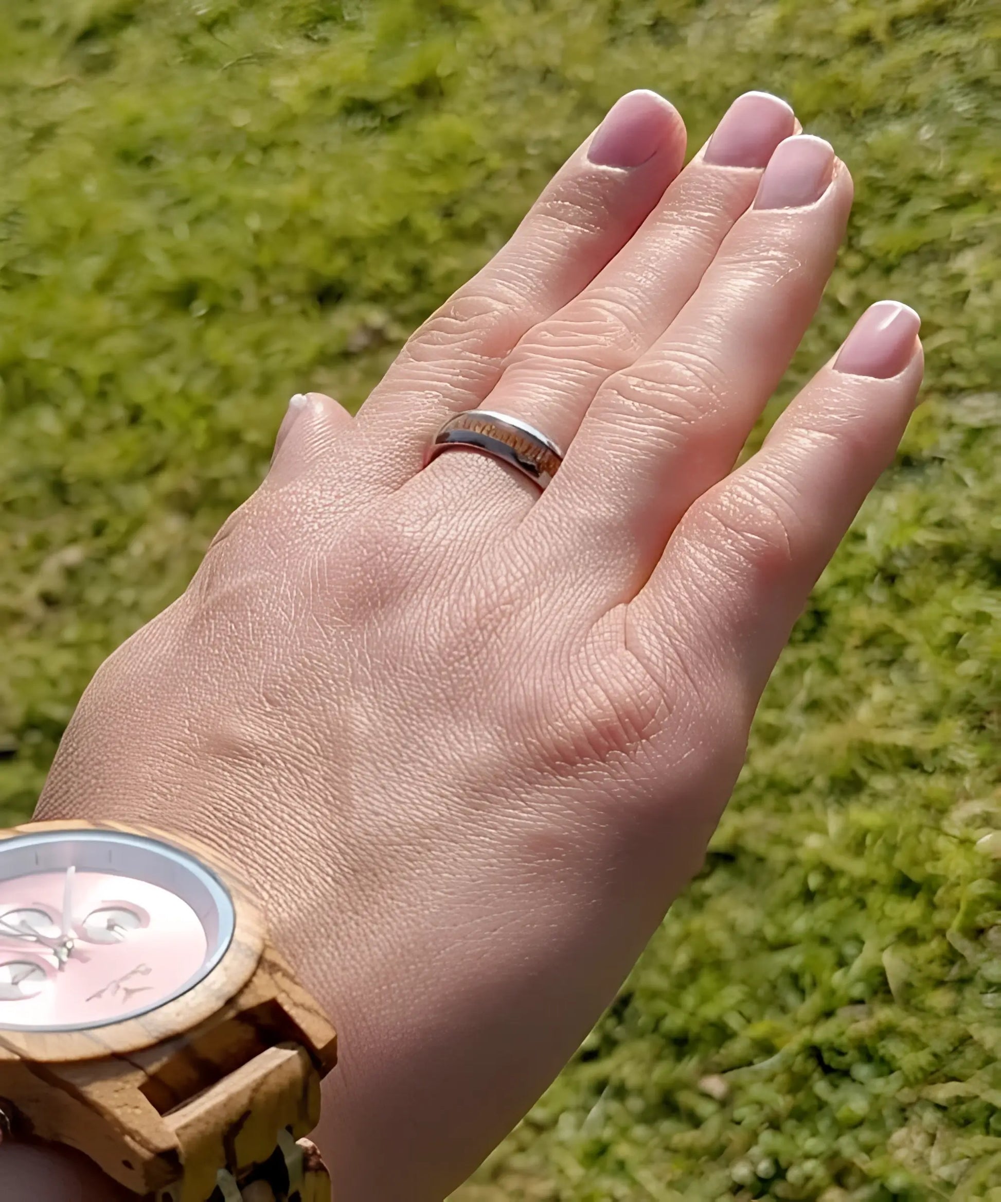 Main de femme portant la bague en bois et argent Elior Klimt, alliance en tungstène argenté avec incrustation de bois raffiné, photographiée en extérieur au soleil.