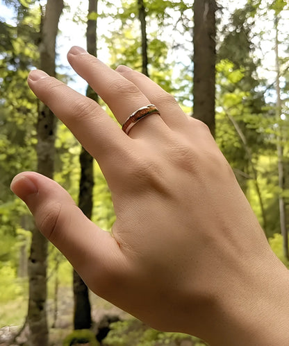 Main d’homme portant la bague en bois et argent Elior Klimt, alliance en tungstène argenté avec incrustation de bois raffiné, photographiée en pleine nature.