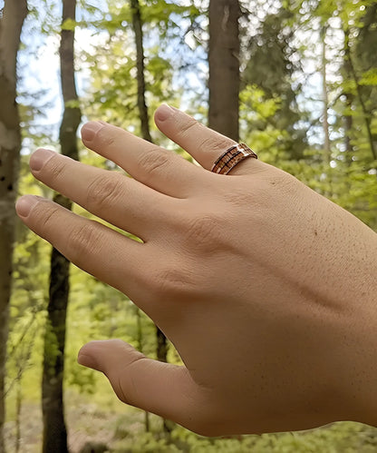 Bague Duo Primordial Adam en tungstène et bois de koa, portée à la main en pleine forêt, alliance élégante et naturelle.