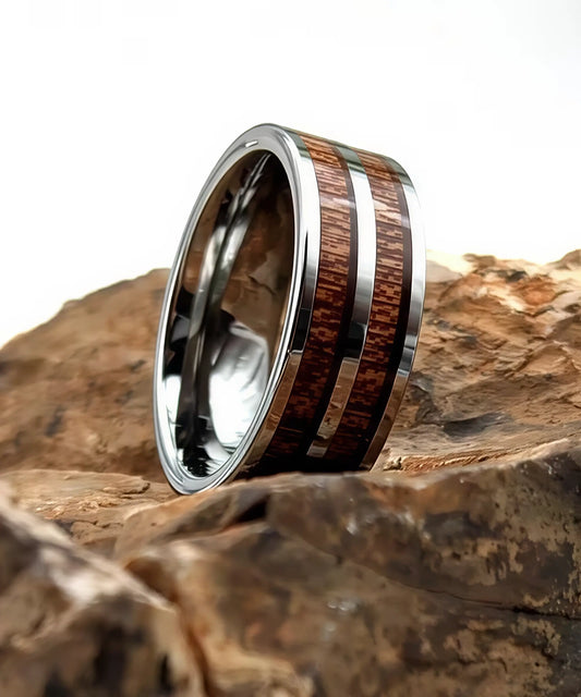 Bague Duo Primordial Adam en tungstène et bois de koa, design moderne à deux bandes de bois, présentée sur roche naturelle.