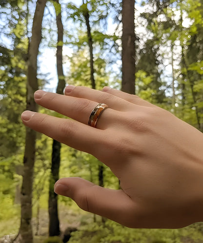 Main portant la bague en bois Flèche de Cupidon argent Passion, anneau en tungstène et bois de koa avec motif flèche, photographié en pleine nature