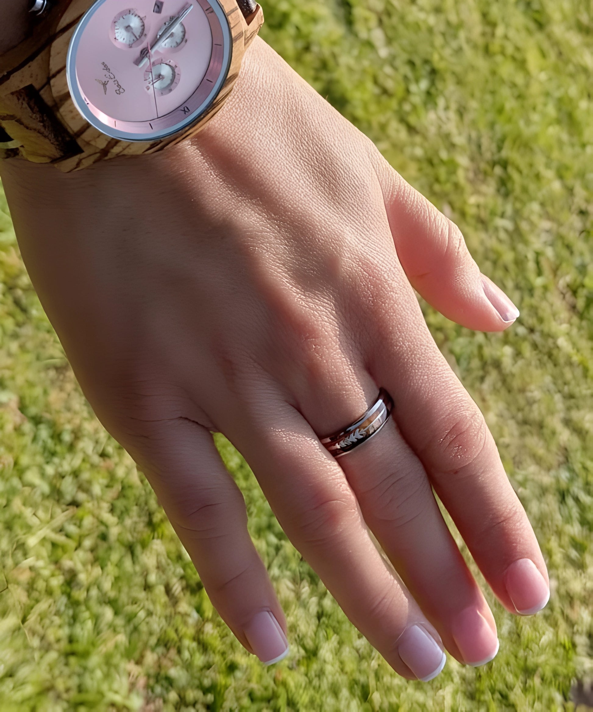 Main de femme portant la bague en bois Flèche de Cupidon Argent Passion Sim, alliance en tungstène argenté avec incrustation bois et motif flèche gravé, photographiée en extérieur.