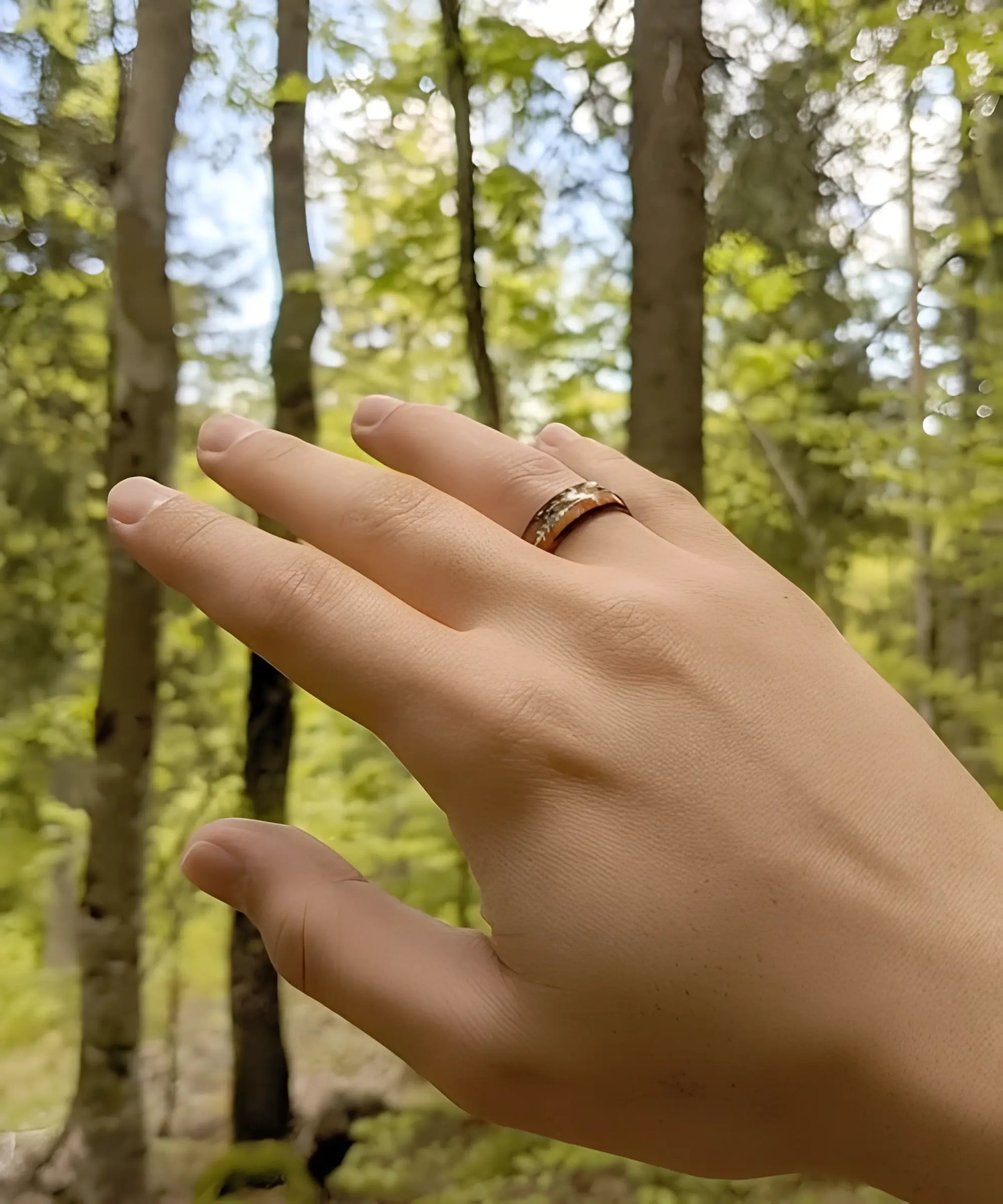 Bague en bois Flèche de Cupidon noire Passion portée à la main en forêt, mettant en valeur ses tons contrastés de bois de koa et son motif flèche argentée.