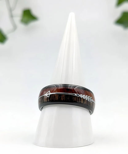Bague Flèche de Cupidon noire Passion en tungstène noir et bois de koa, ornée d’une flèche argentée, présentée sur un cône blanc élégant.