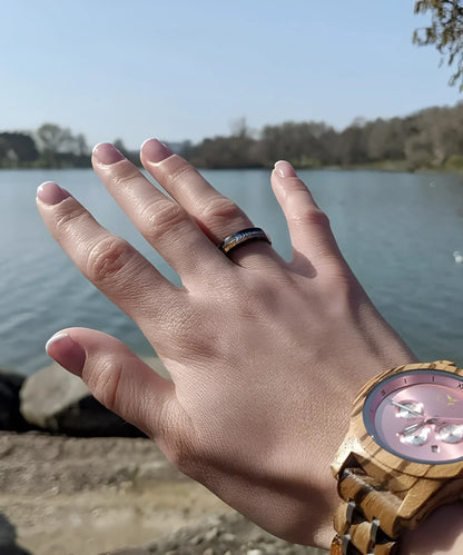 Bague en bois Flèche de Cupidon noire Passion Sim 6 mm en tungstène noir avec incrustation de bois de koa et flèche argentée, portée à la main près d’un lac avec une montre en bois.