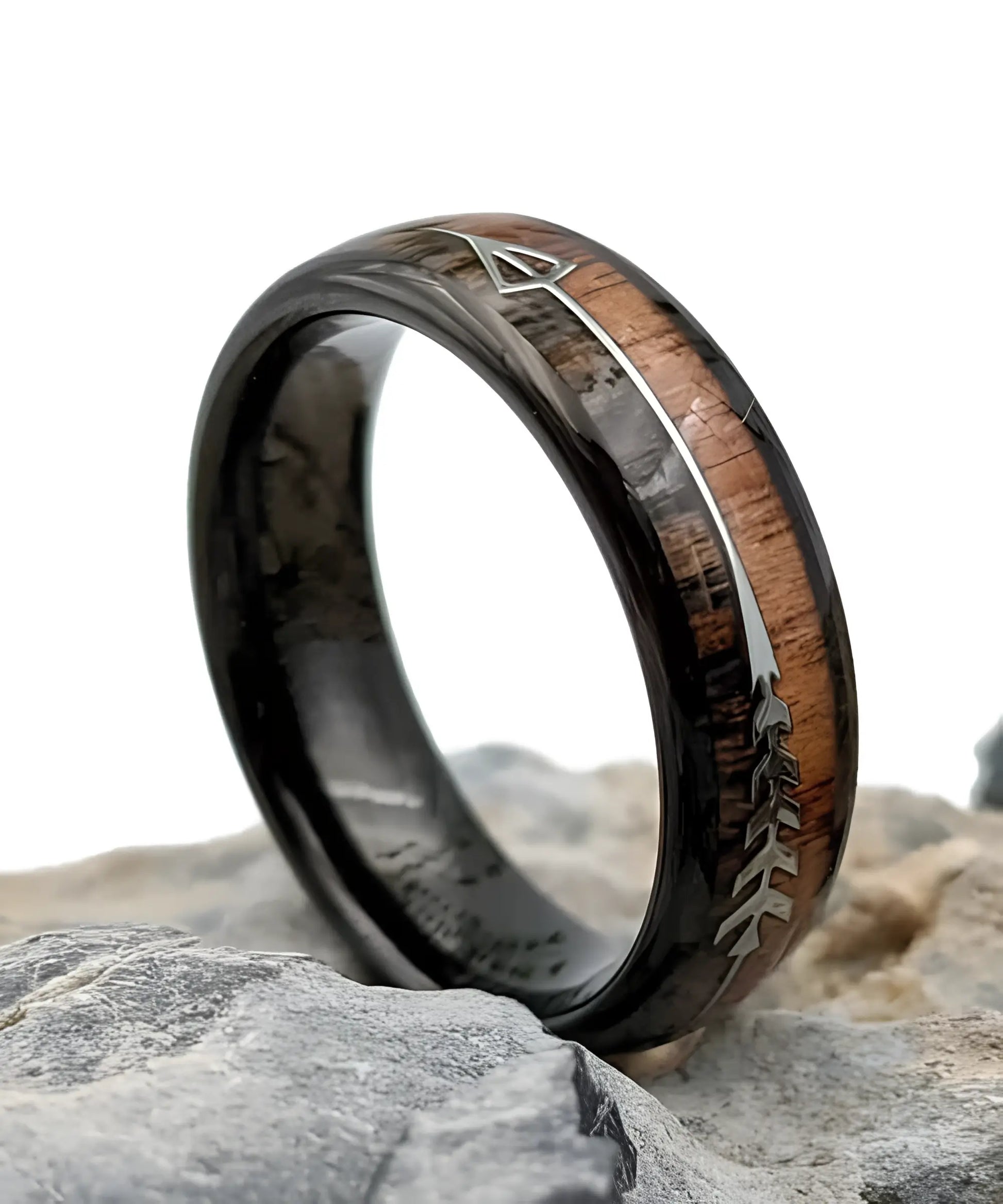 Bague en bois Flèche de Cupidon noire Passion Sim en version 6 mm, anneau en tungstène noir avec bois de koa clair et sombre, motif flèche argentée, posée sur des roches.