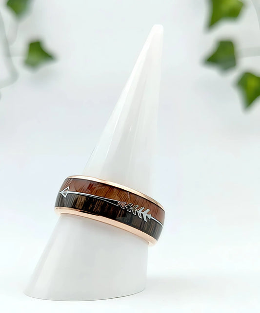 Bague en bois Flèche de Cupidon Rose Passion en tungstène doré rose, alliance incrustée de bois naturel et flèche argentée, présentée sur support blanc en studio