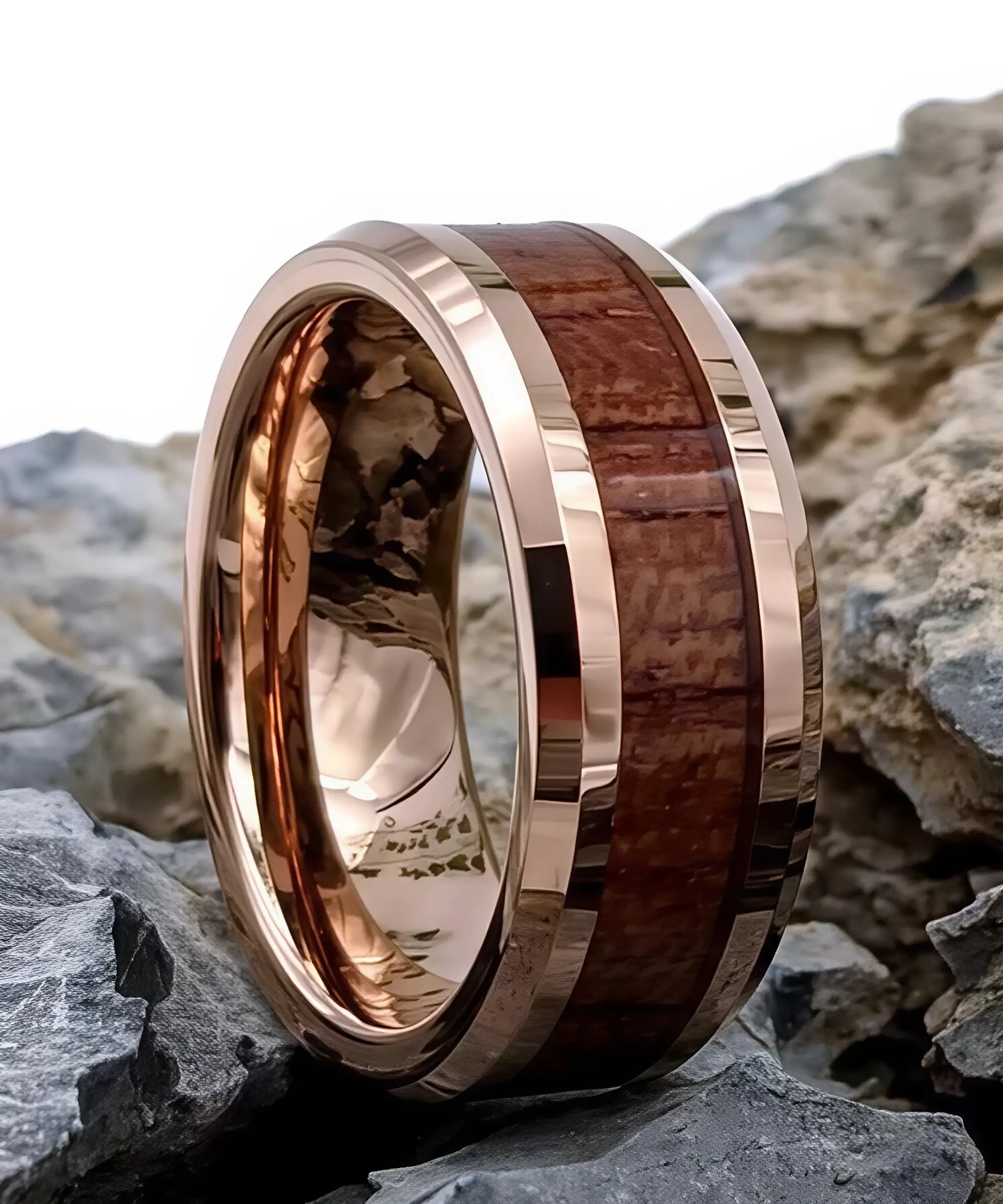 Bague en bois de koa incrustée dans un anneau en tungstène or rose, posée sur des roches naturelles.
