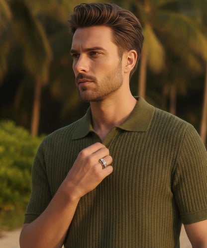 Homme en gros plan tenant son col de polo vert, mettant en avant la Bague Duo d’Eden au coucher du soleil sur la plage.