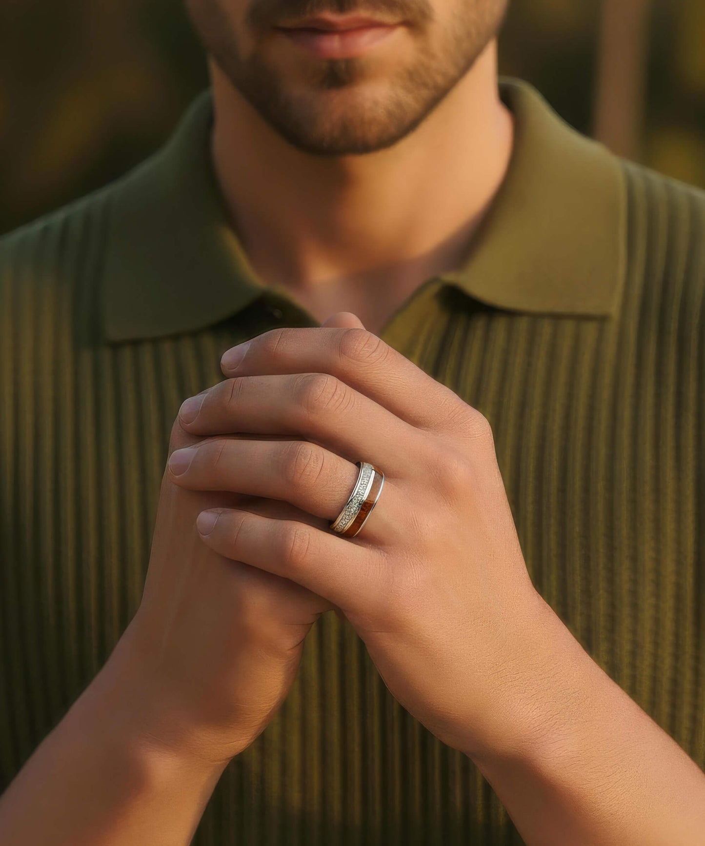 Gros plan sur les mains d’un homme entrelacées portant la Bague Duo d’Eden, avec un polo vert en arrière-plan.