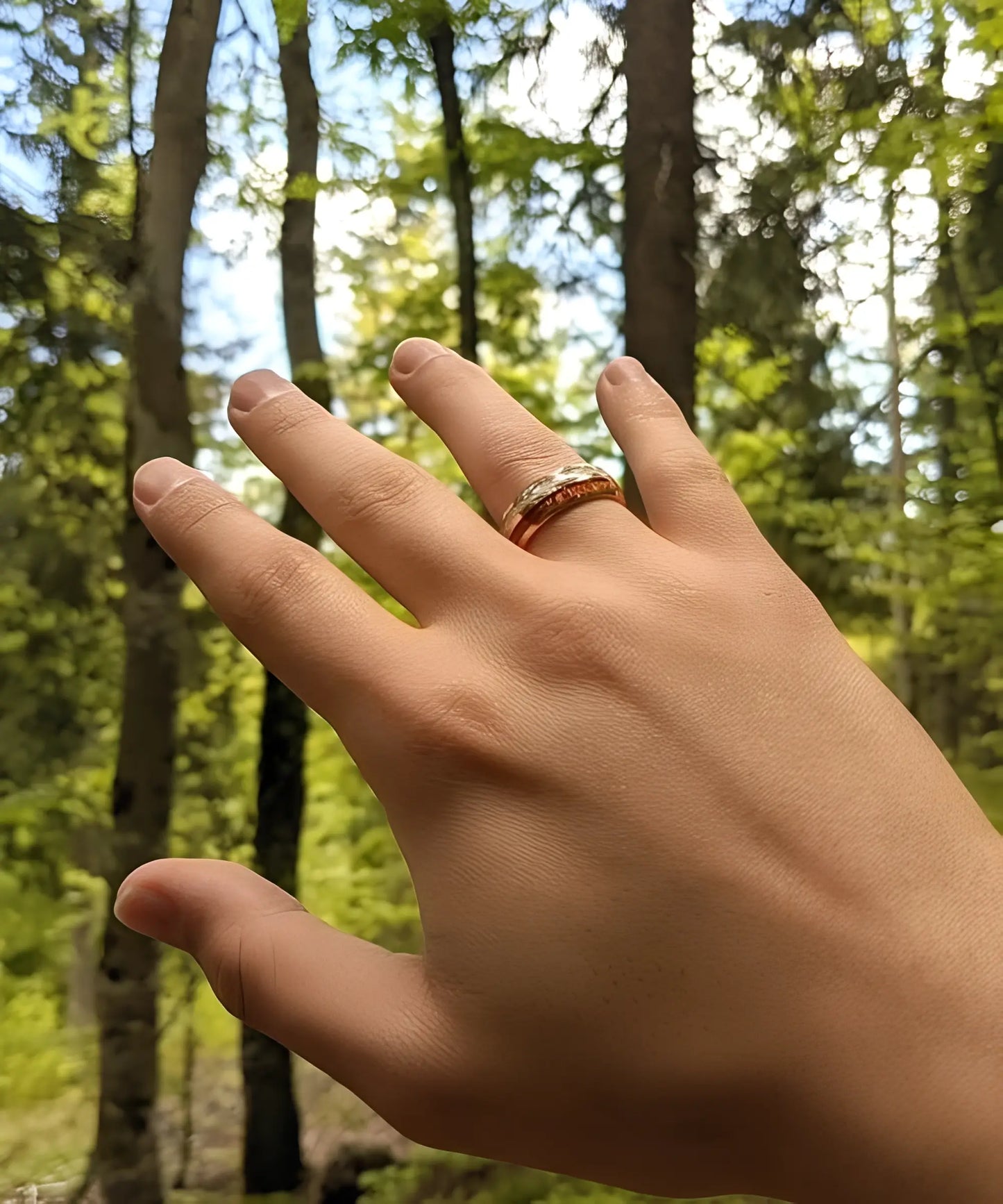 Main portant la bague Duo d’Eden en tungstène doré et bois de koa, photographiée en pleine nature avec un fond forestier