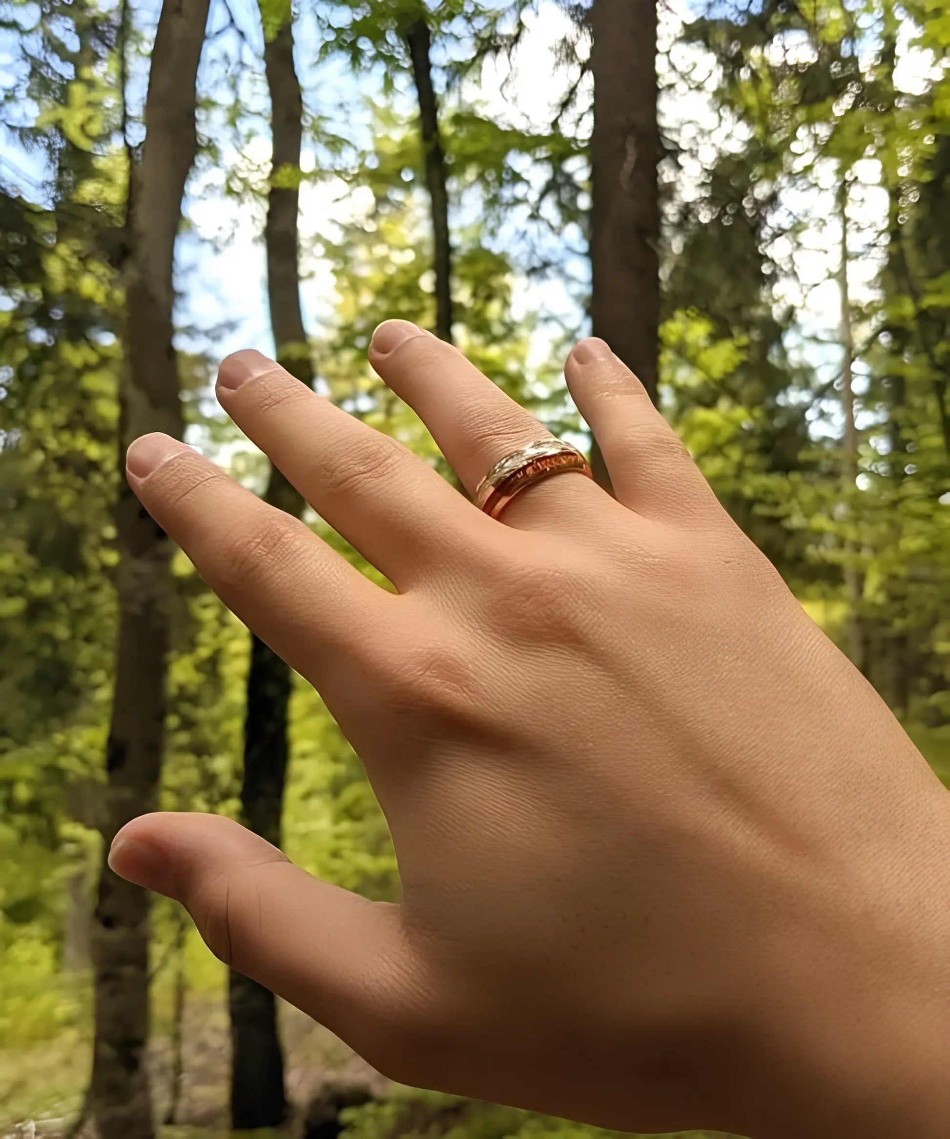 Main portant la bague Duo d’Eden en tungstène doré et bois de koa, photographiée en pleine nature avec un fond forestier