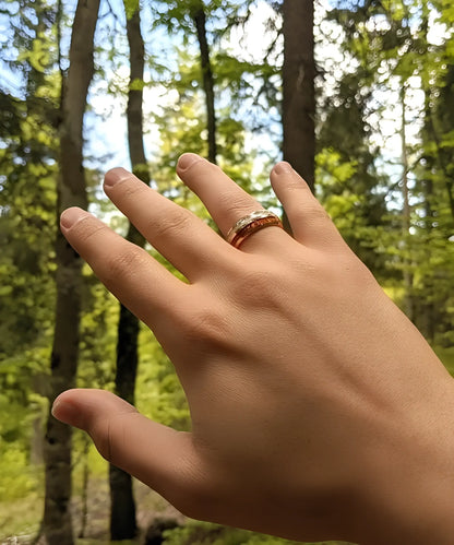 Main portant la bague Duo d’Eden en tungstène doré et bois de koa, photographiée en pleine nature avec un fond forestier