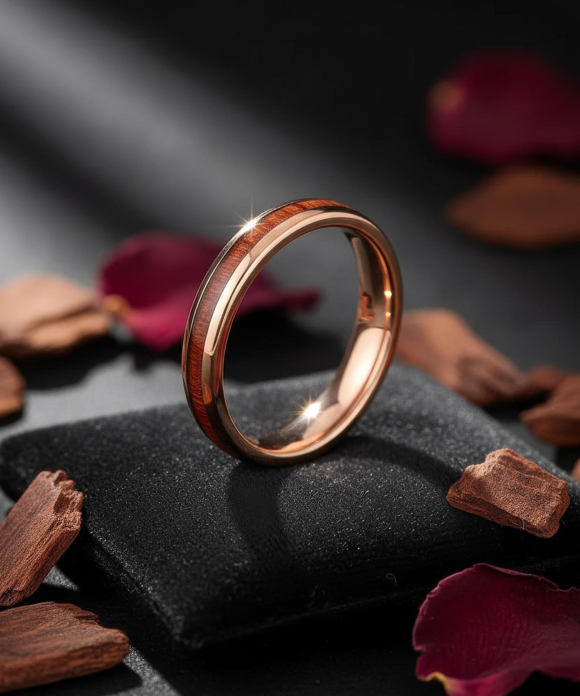 Alliance Elior Rose en bois et métal doré, posée sur un coussin noir avec pétales et éclats de bois sous une lumière douce