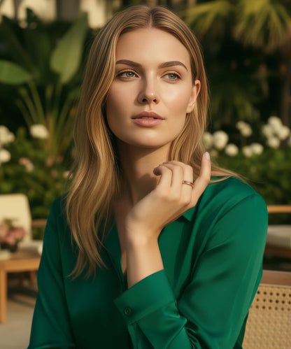 Femme élégante portant la bague Elior Rose en bois et métal doré, assise dans un jardin d’hôtel raffiné, vêtue d’une chemise verte satinée