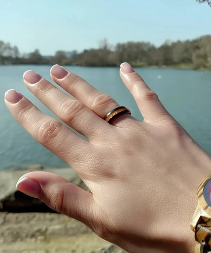Bague en bois Elior Klimt noire portée en extérieur, main avec incrustation bois marron mise en valeur au bord d’un lac