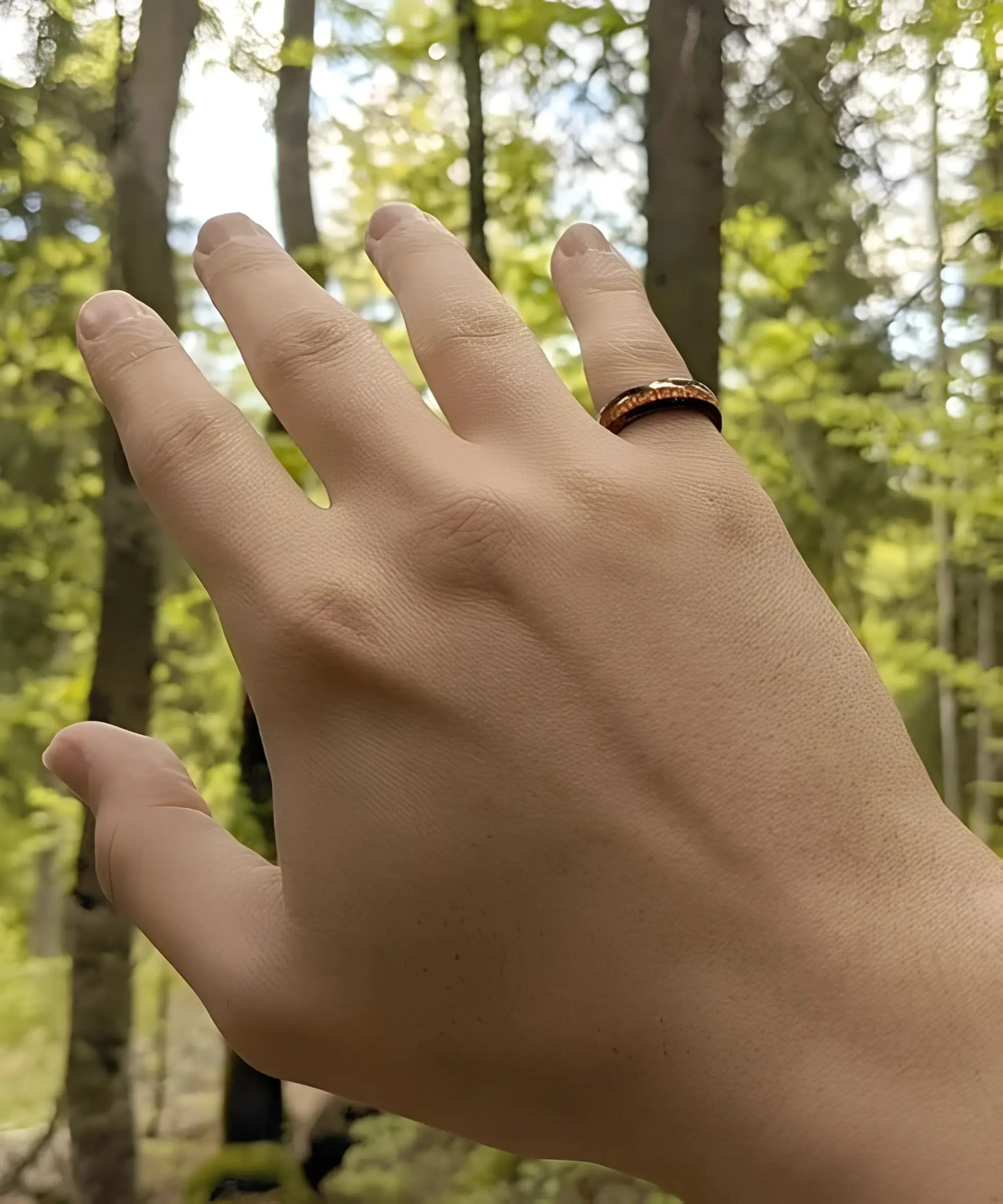 Bague en bois Elior Klimt noire portée à la main, incrustation en bois naturel mise en valeur en pleine forêt