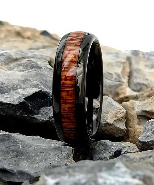 Bague en bois Elior Klimt noire, anneau en tungstène poli avec incrustation de bois marron foncé, posée sur des roches naturelles
