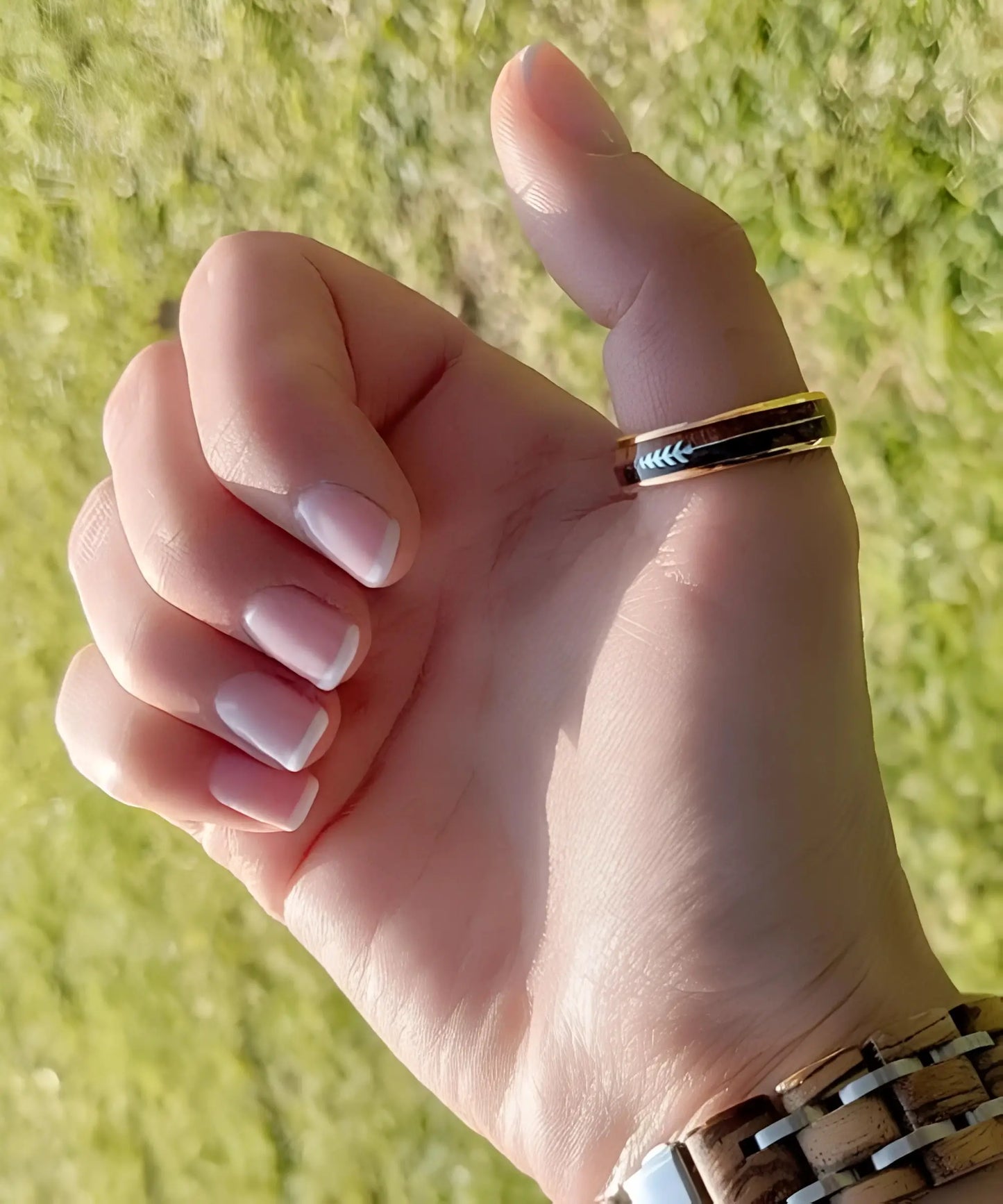 Bague en bois Flèche de Cupidon rose Passion Sim portée au pouce, anneau en tungstène or rose avec incrustation bois et flèche gravée, en extérieur ensoleillé