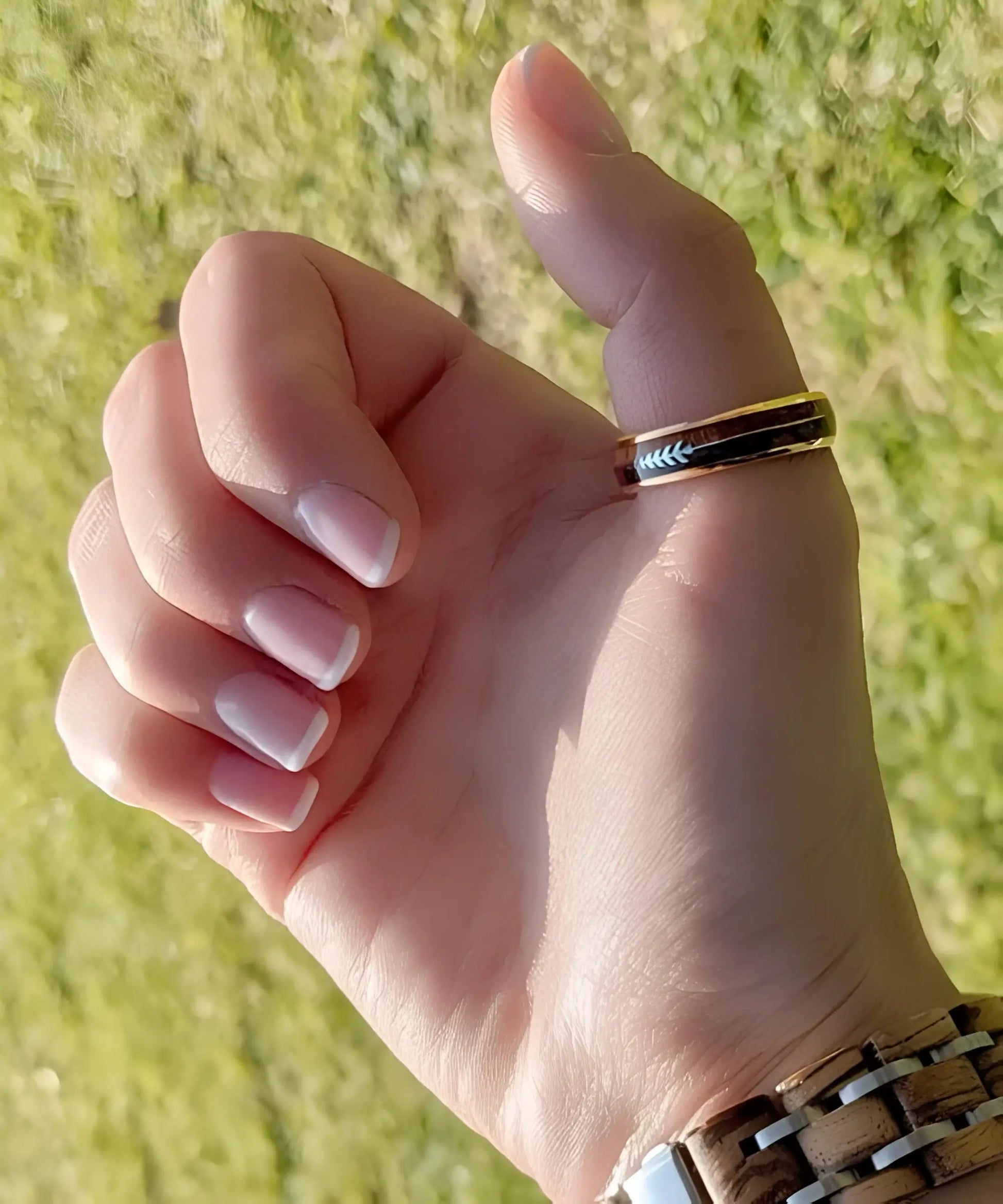 Bague en bois Flèche de Cupidon rose Passion Sim portée au pouce, anneau en tungstène or rose avec incrustation bois et flèche gravée, en extérieur ensoleillé