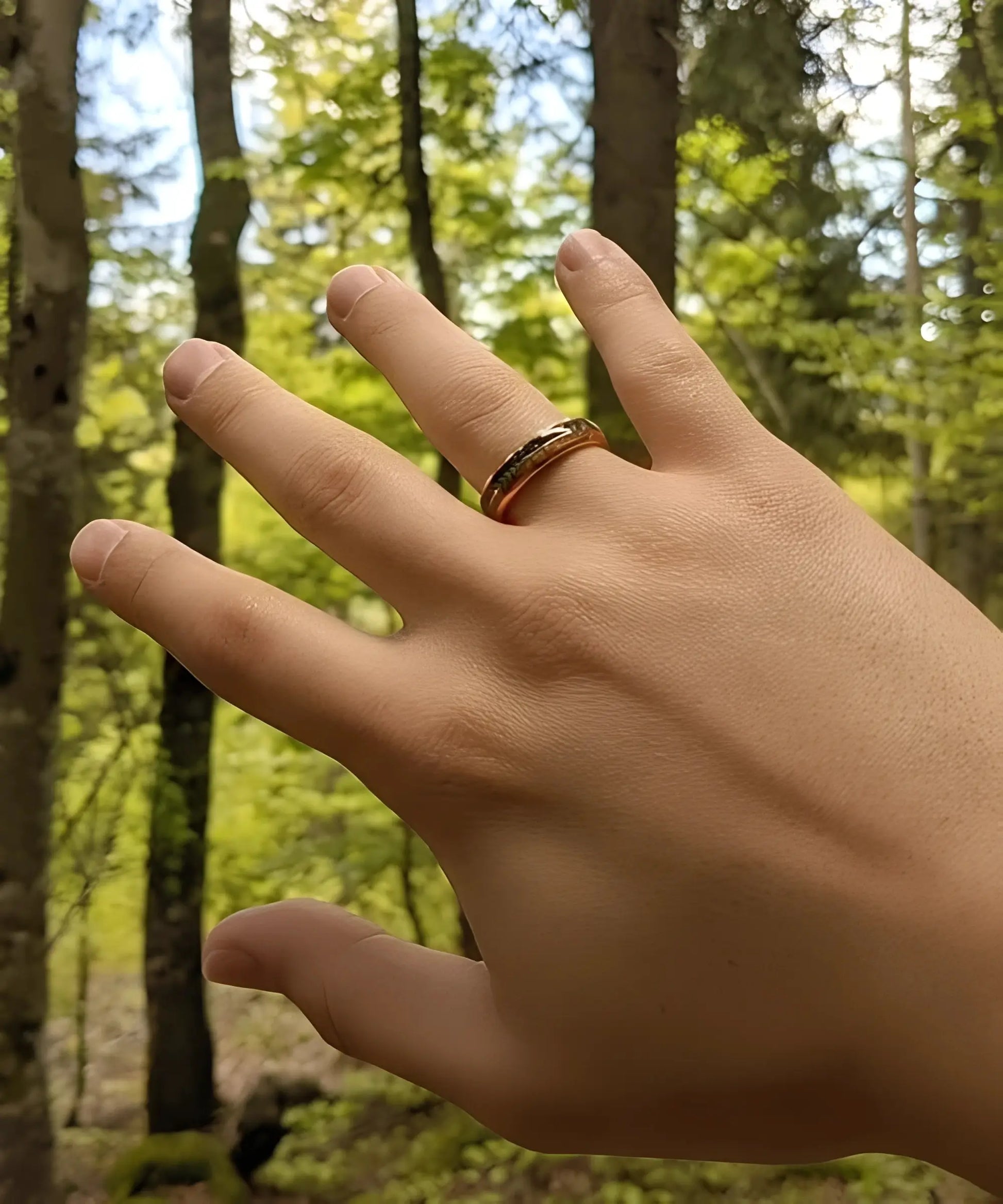Bague en bois Flèche de Cupidon rose Passion Sim portée à la main, anneau en tungstène or rose avec incrustation bois et motif flèche, en extérieur forêt