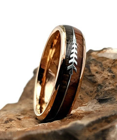 Bague en bois Flèche de Cupidon rose Passion Sim, anneau en tungstène or rose avec incrustation bois naturel et motif flèche, posée sur une roche