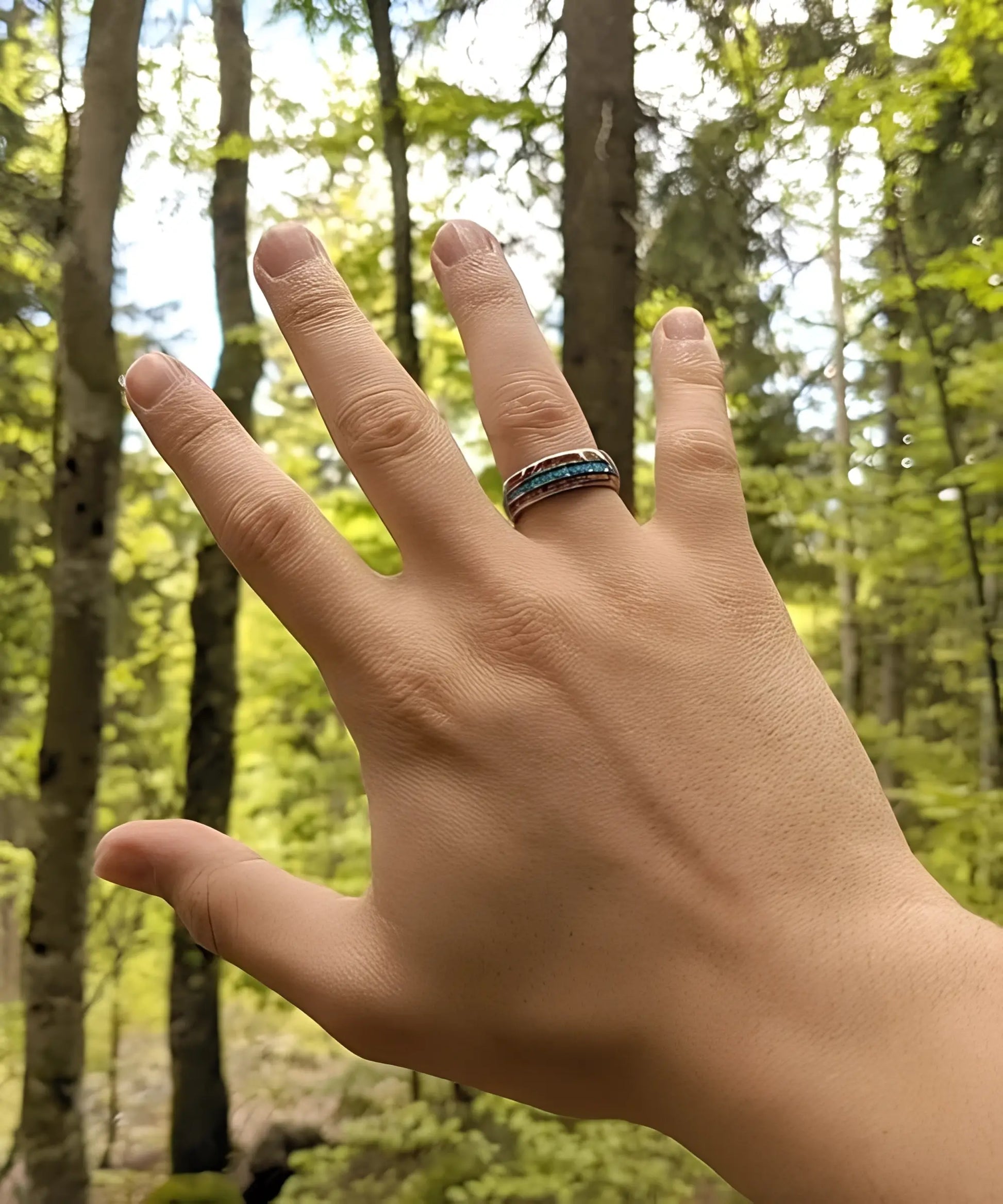 Main portant la bague en bois Ark Upto en tungstène avec deux bandes de koa et une incrustation bleue, en pleine forêt