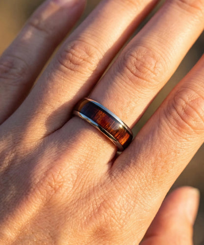 Bague homme en bois Ouranos argent portée sur une main, alliance en tungstène argent avec incrustation de bois naturel éclairée par une lumière chaude.