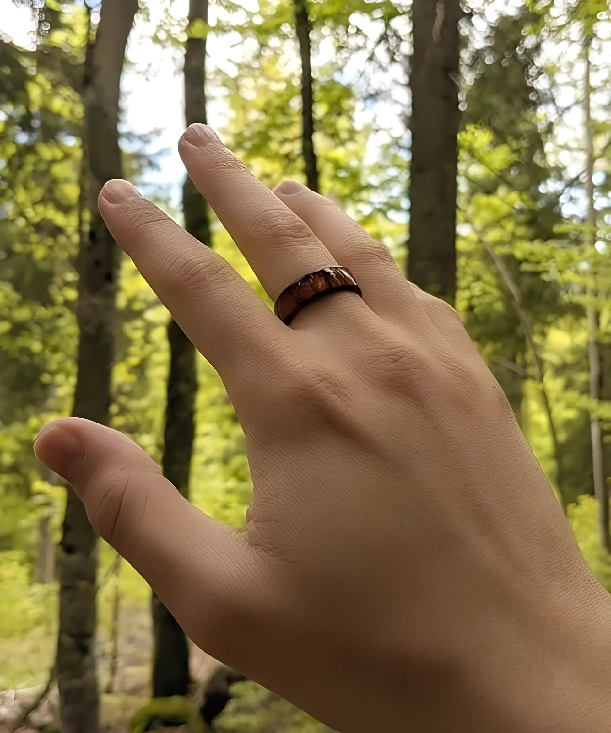 Main portant la bague Ouranos noire en tungstène et bois de koa, mise en valeur dans une forêt verdoyante.