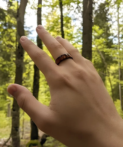 Main portant la bague Ouranos noire en tungstène et bois de koa, mise en valeur dans une forêt verdoyante.