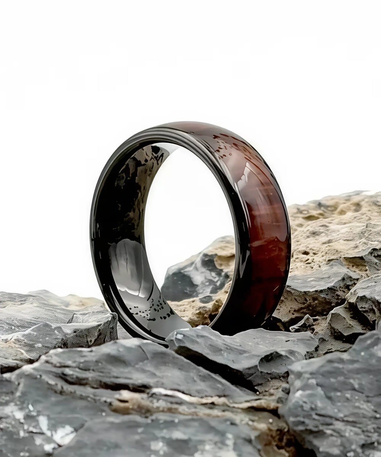 Bague Ouranos noire en tungstène et bois de koa posée sur des pierres, alliance élégante entre robustesse et naturel
