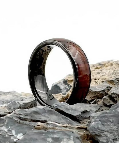 Bague Ouranos noire en tungstène et bois de koa posée sur des pierres, alliance élégante entre robustesse et naturel