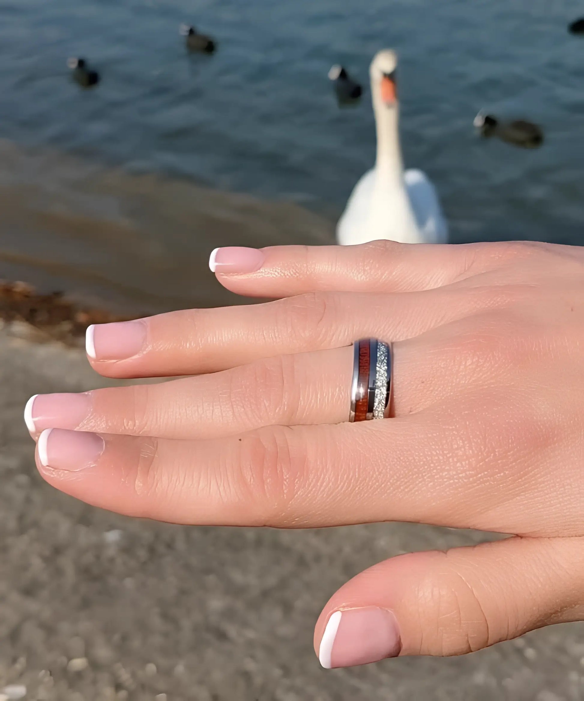 Bague en tungstène avec incrustation de bois de koa et bande aspect météorite portée à la main, style moderne et raffiné.