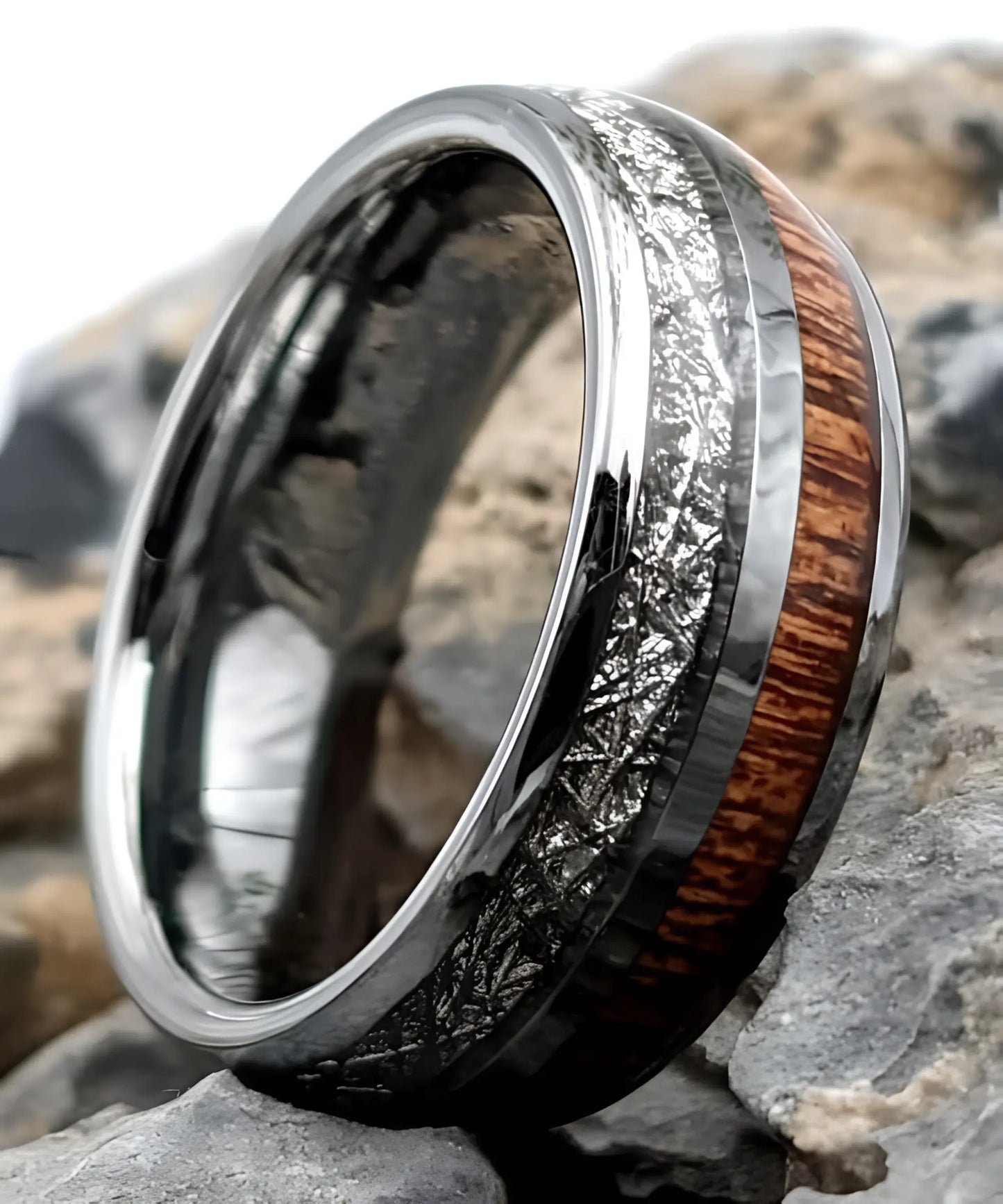 Bague en tungstène avec incrustation de bois de koa et bande aspect météorite posée sur des pierres, bijou moderne et élégant.