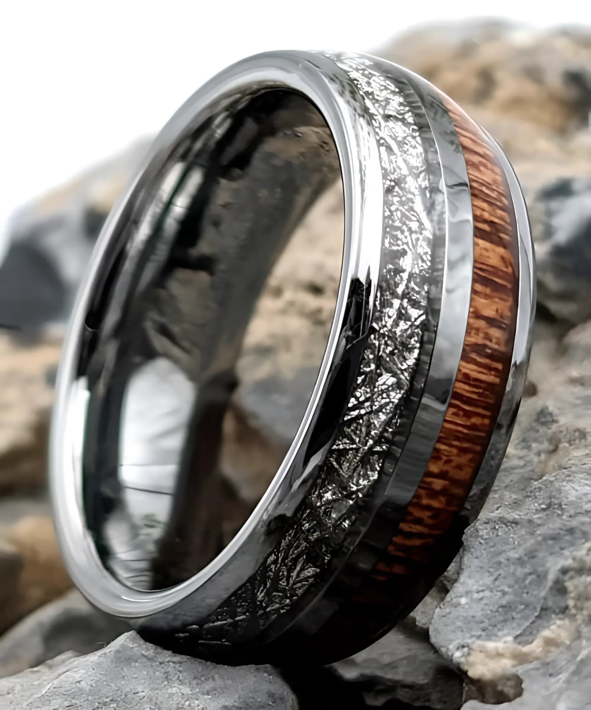 Bague en tungstène avec incrustation de bois de koa et bande aspect météorite posée sur des pierres, bijou moderne et élégant.