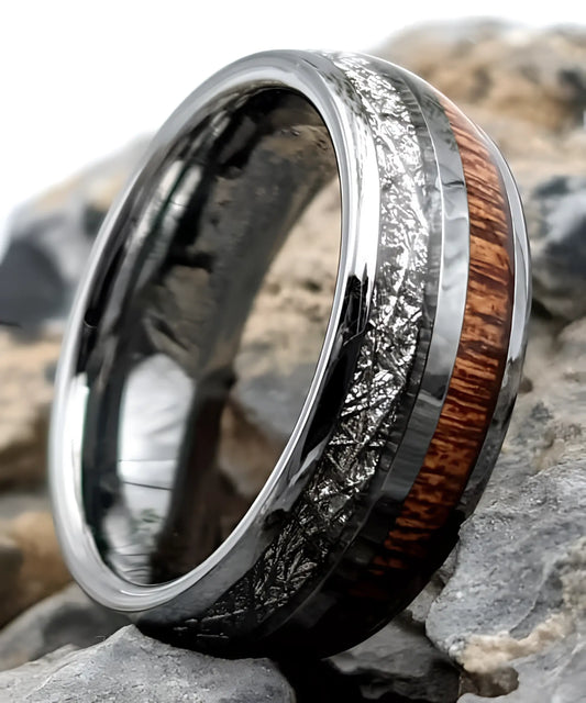 Bague en tungstène avec incrustation de bois de koa et bande aspect météorite posée sur des pierres, bijou moderne et élégant.