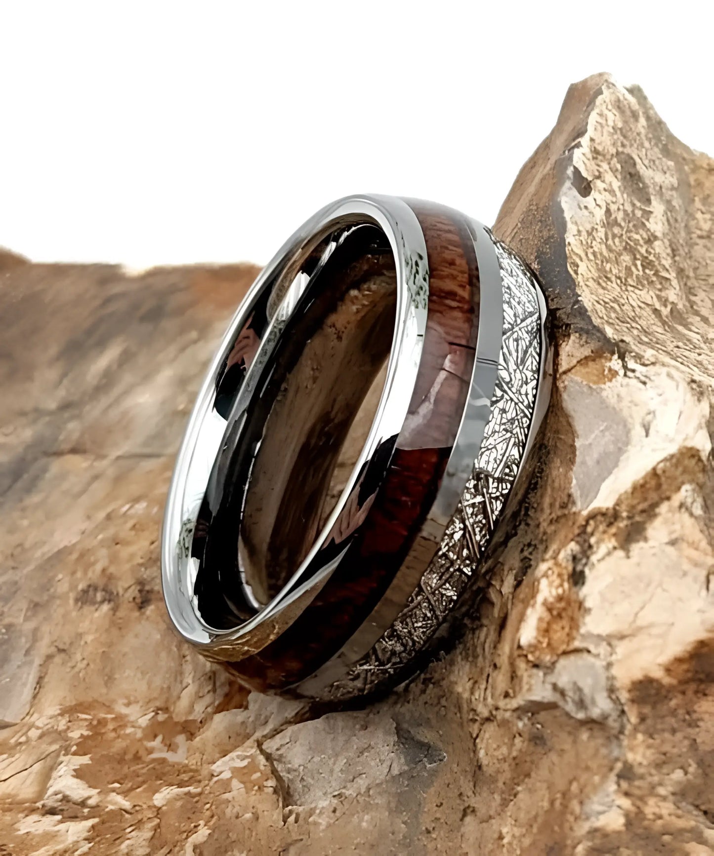 Bague en tungstène avec incrustation de bois de koa et bande aspect météorite posée sur une roche, design élégant et naturel.