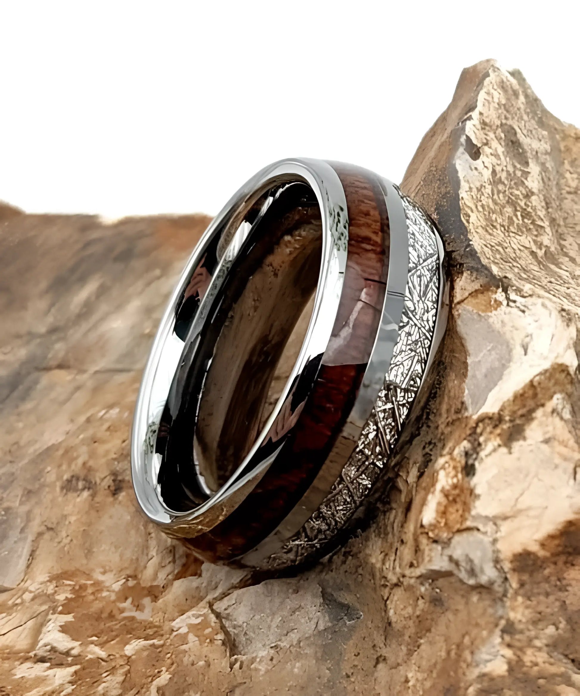 Bague en tungstène avec incrustation de bois de koa et bande aspect météorite posée sur une roche, design élégant et naturel.