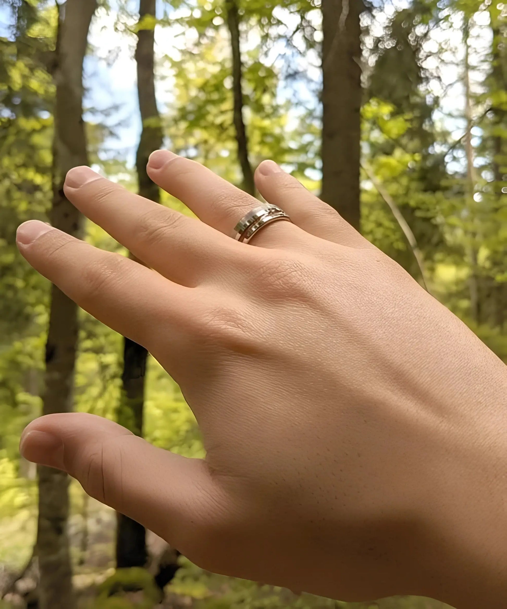Bague Ultron argent en tungstène poli et brossé avec incrustation de bois de koa, portée au doigt dans un cadre naturel en forêt