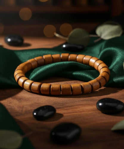Bracelet en bois naturel Orion avec perles carrées, présenté sur un tissu vert et un décor en bois, ambiance élégante et chaleureuse.